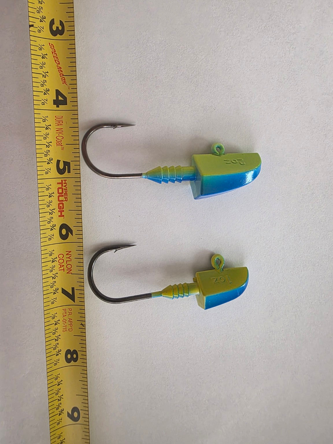 Blue Green 1 ounce and 2 ounce lead jig heads beside a measuring tape